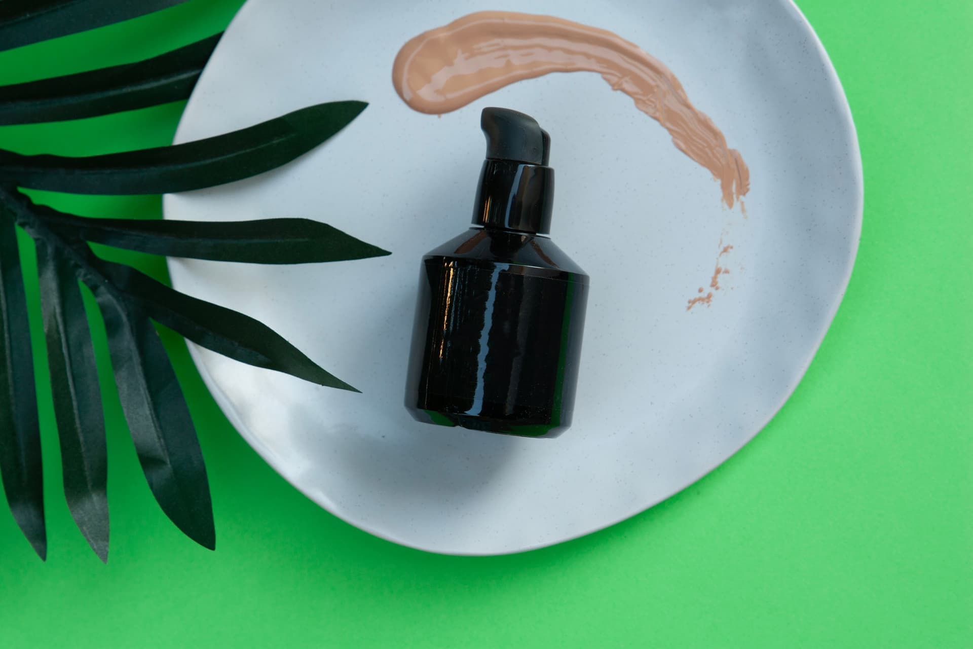 A plain pump bottle on a white dish with a smear of makeup beside it