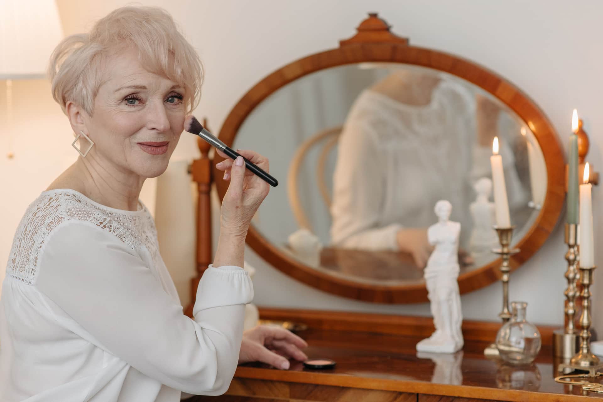 A senior woman applying makeup with a brush beside a mirror