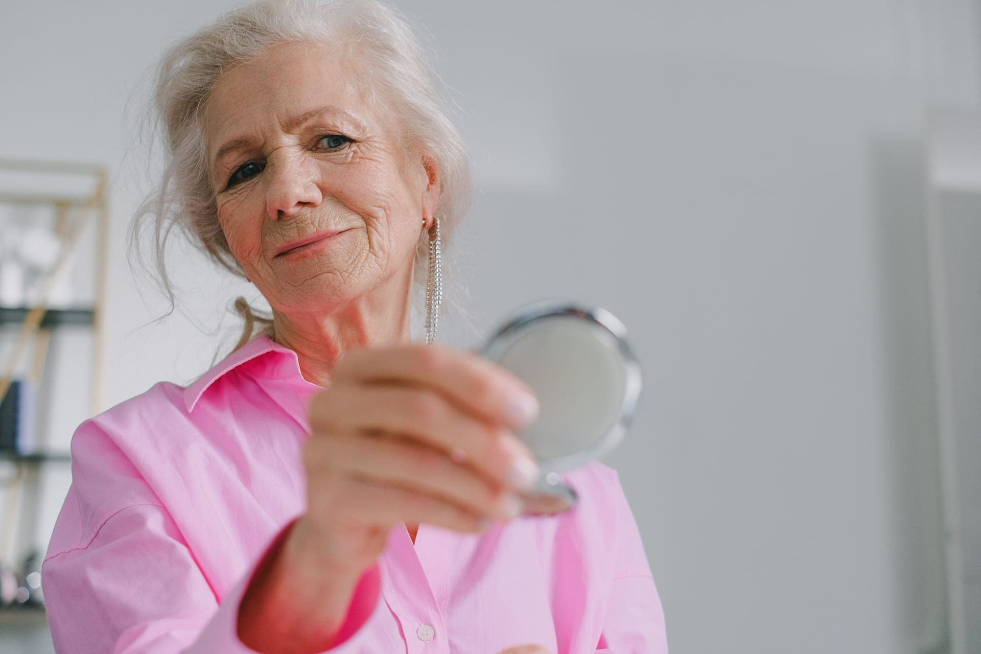 An older woman holding a compact mirror indoors