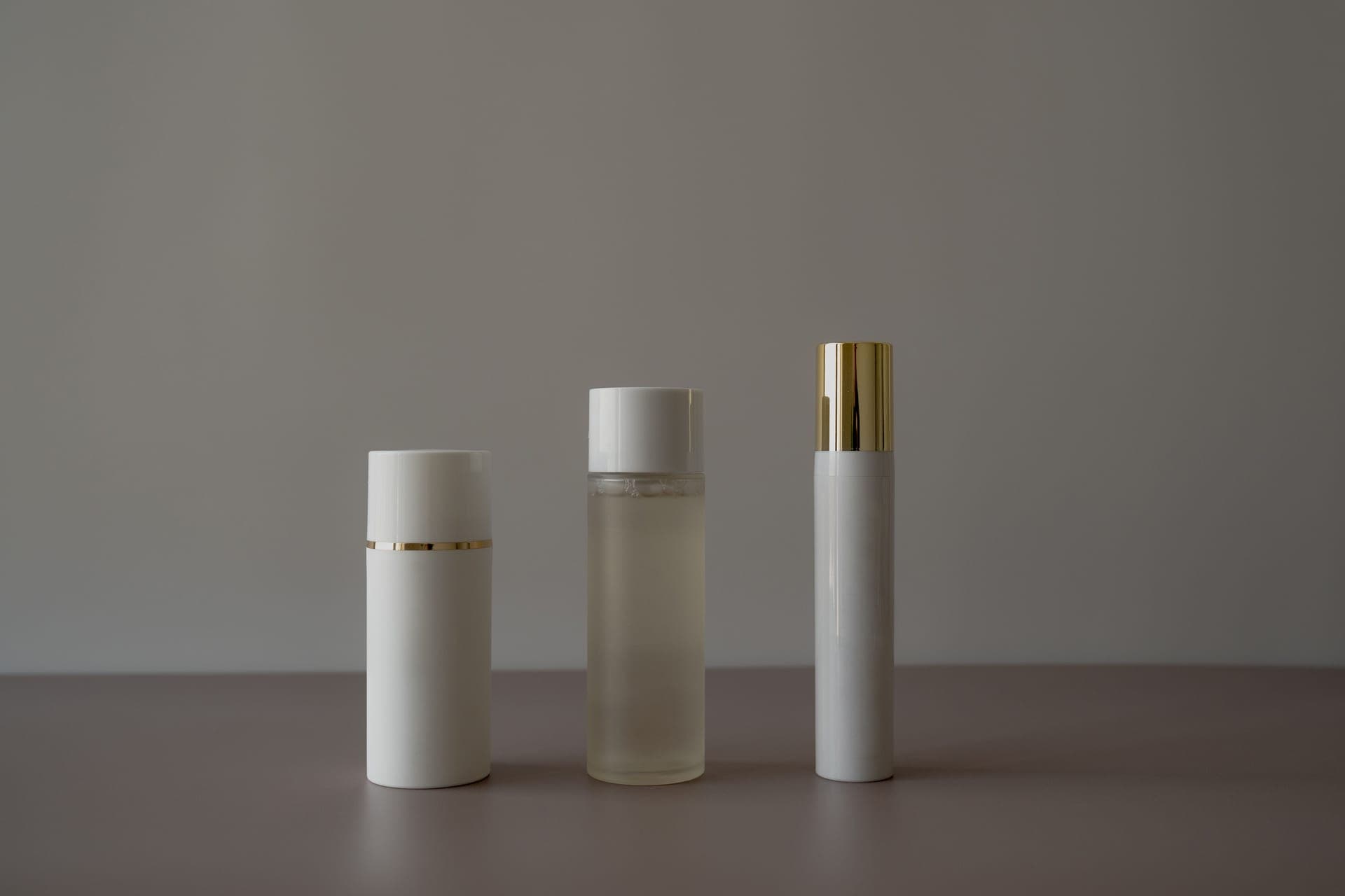 A minimal arrangement of plain cosmetic bottles on a gray background