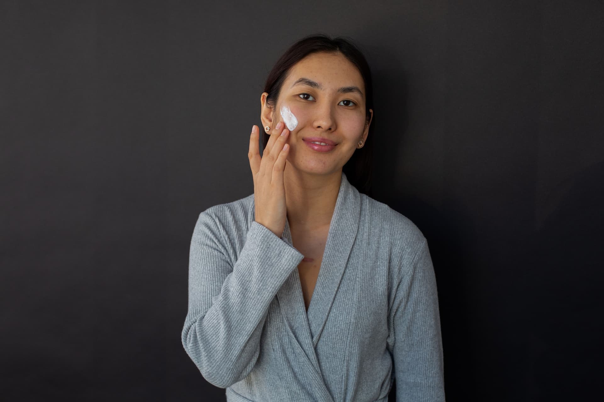 A woman applying moisturizer to her cheek during a daily skincare routine